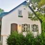 White house with green shutters, surrounded by trees.