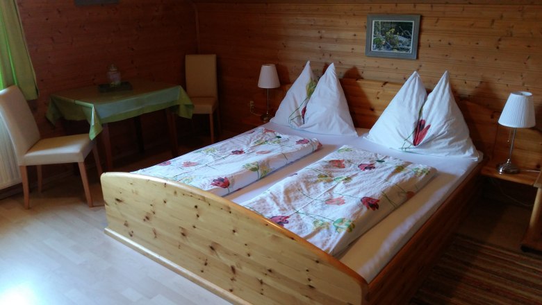 Cozy room with wooden walls, double bed and table at the Wachabauer farm.