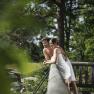 A couple in towels lean against a wooden railing in a green, wooded setting.