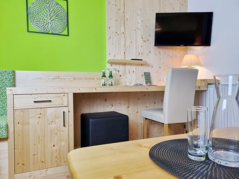 A hotel room with wooden furniture, a desk, a TV on the wall and green wall decorations.