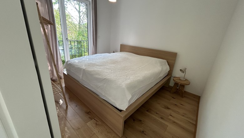 Bedroom with wooden floor, double bed and window with view of the greenery.