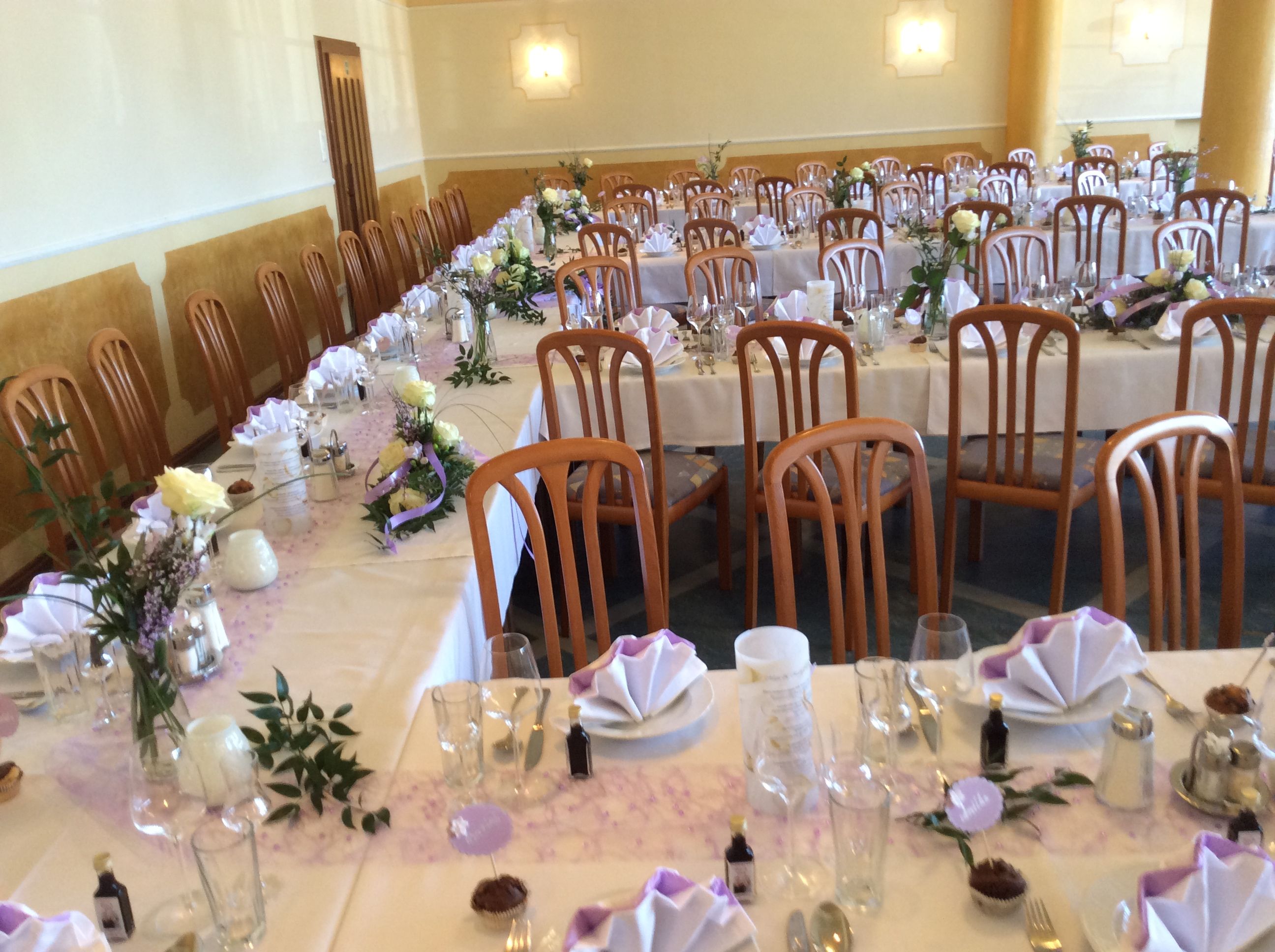 Festively laid hall with long tables, decorated with flowers and folded napkins.