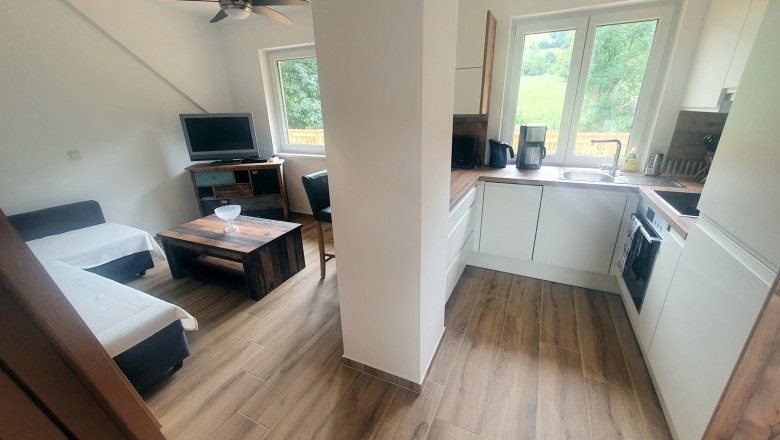 Modern eat-in kitchen with wooden floor, sofa, TV and kitchenette.