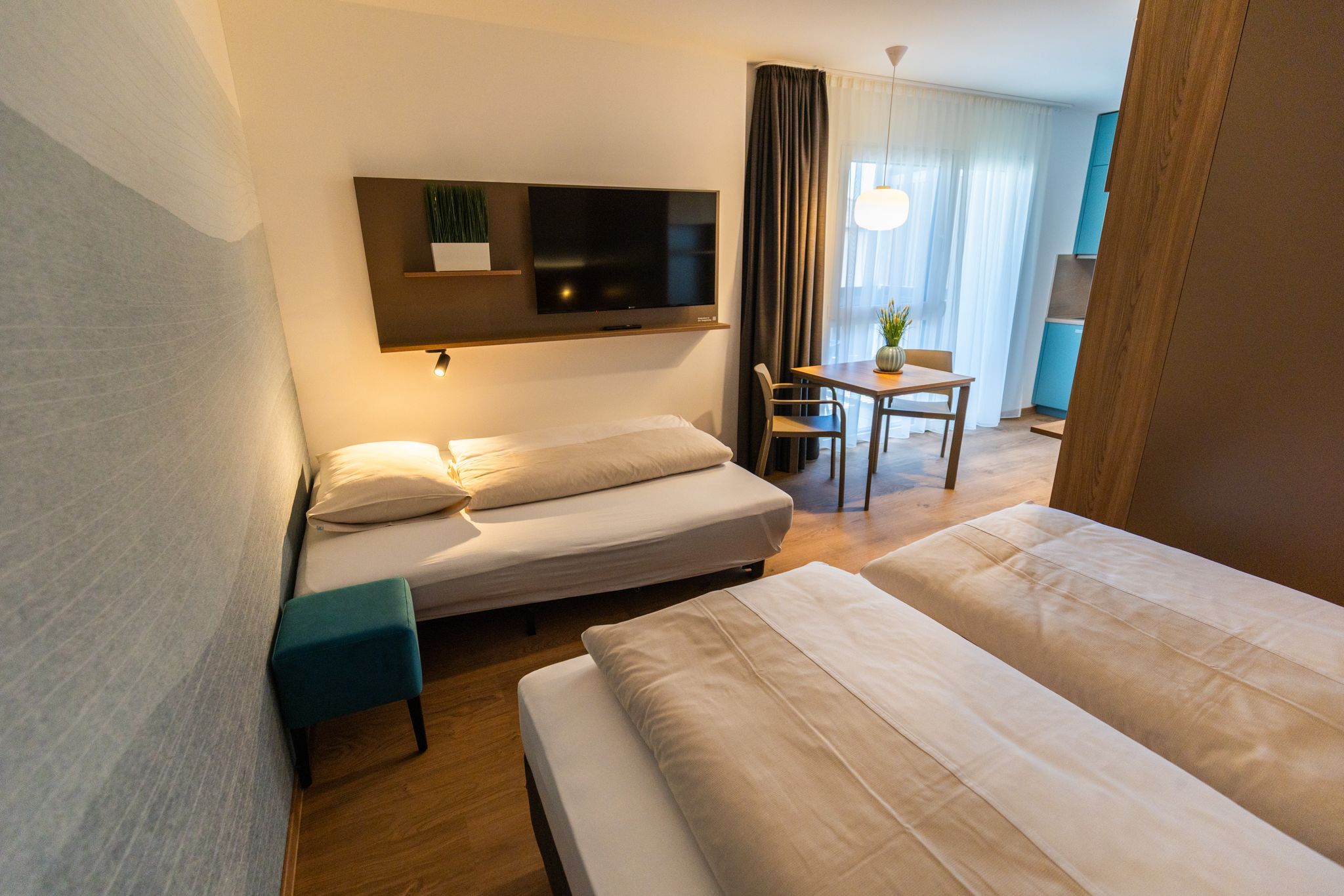 A modern hotel room with two beds, a table, and a TV mounted on the wall.