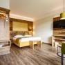 Modern hotel room with wooden furniture, double bed, green armchair and flat screen TV.