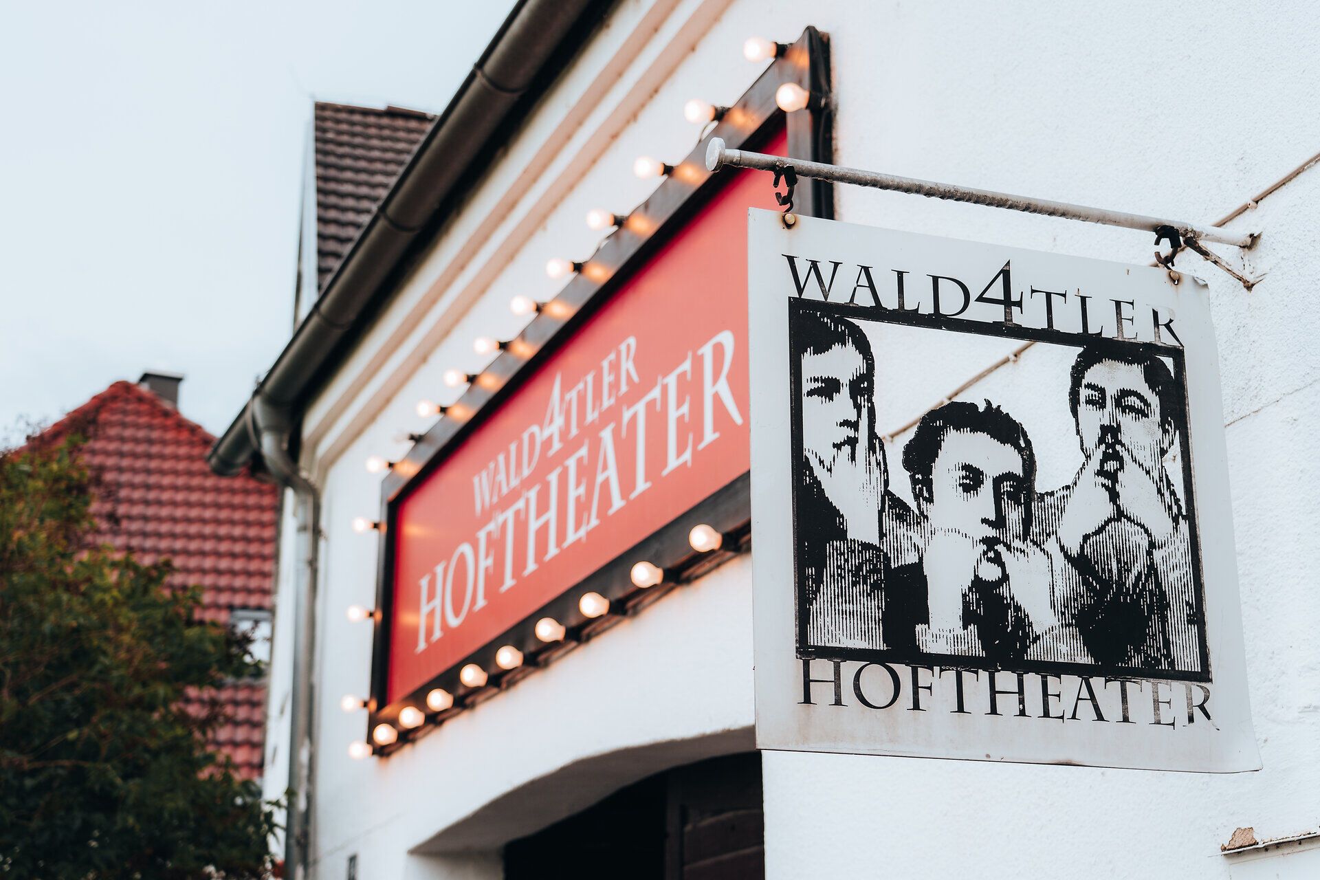 Exterior view of the Wald4tler Hoftheater with illuminated sign and a picture of three people.