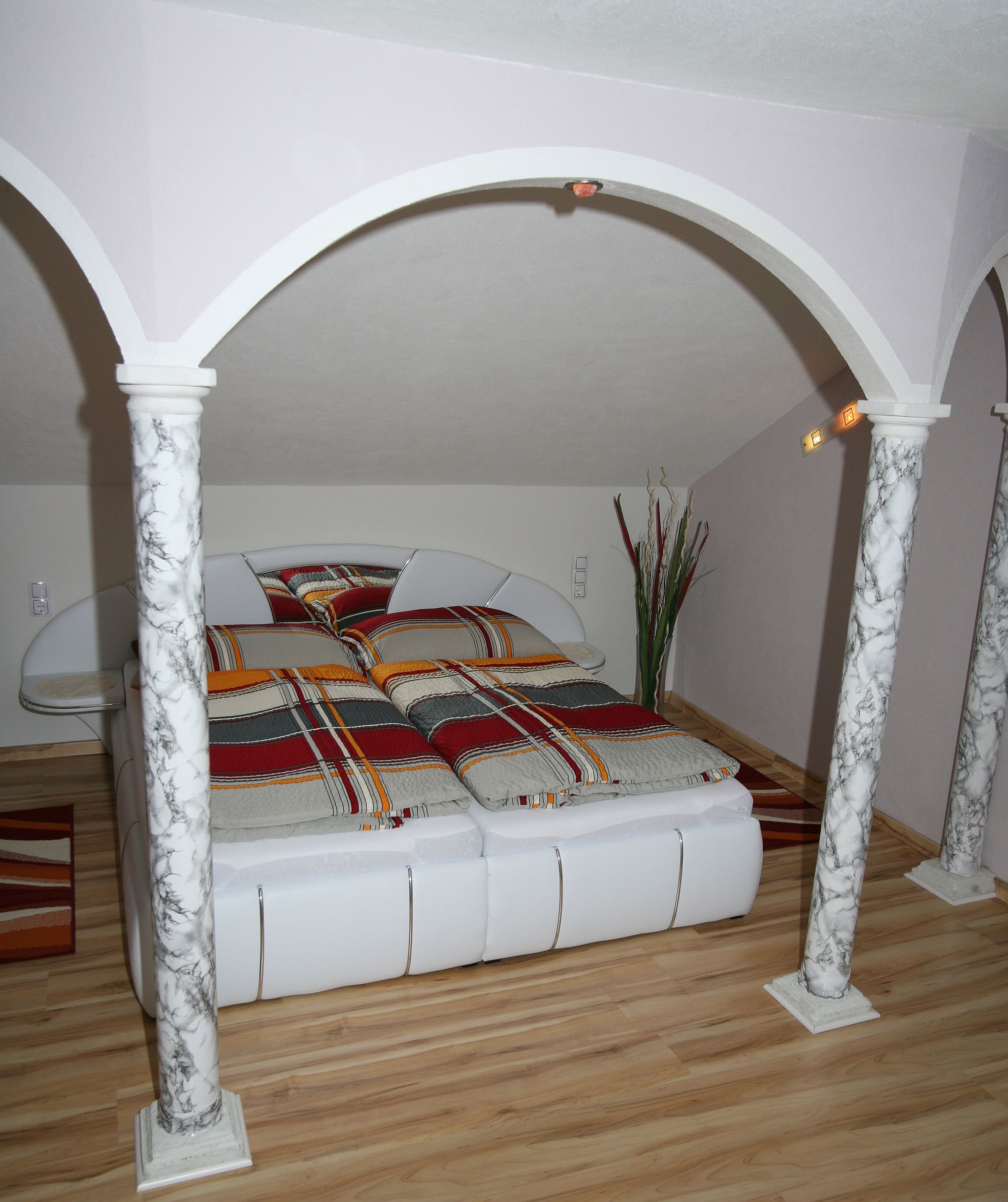 Bedroom with double bed, marble pillars and striped bed linen.