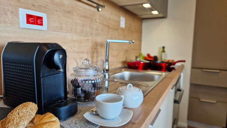 Modern kitchen with coffee machine, bread rolls and crockery on the worktop.