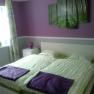 Bedroom with purple and green decoration, double bed, bedside table and window.