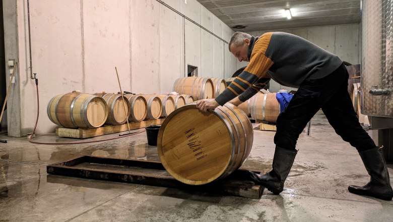 A person rolls a wooden barrel in a wine cellar.