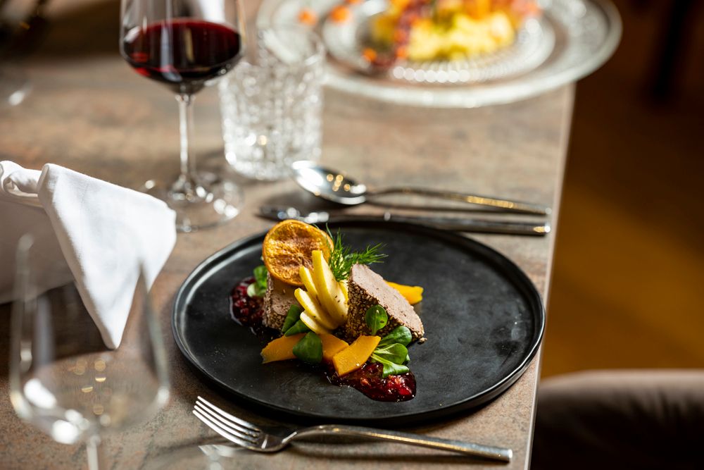 Gourmet dish on a black plate with red wine in the background.