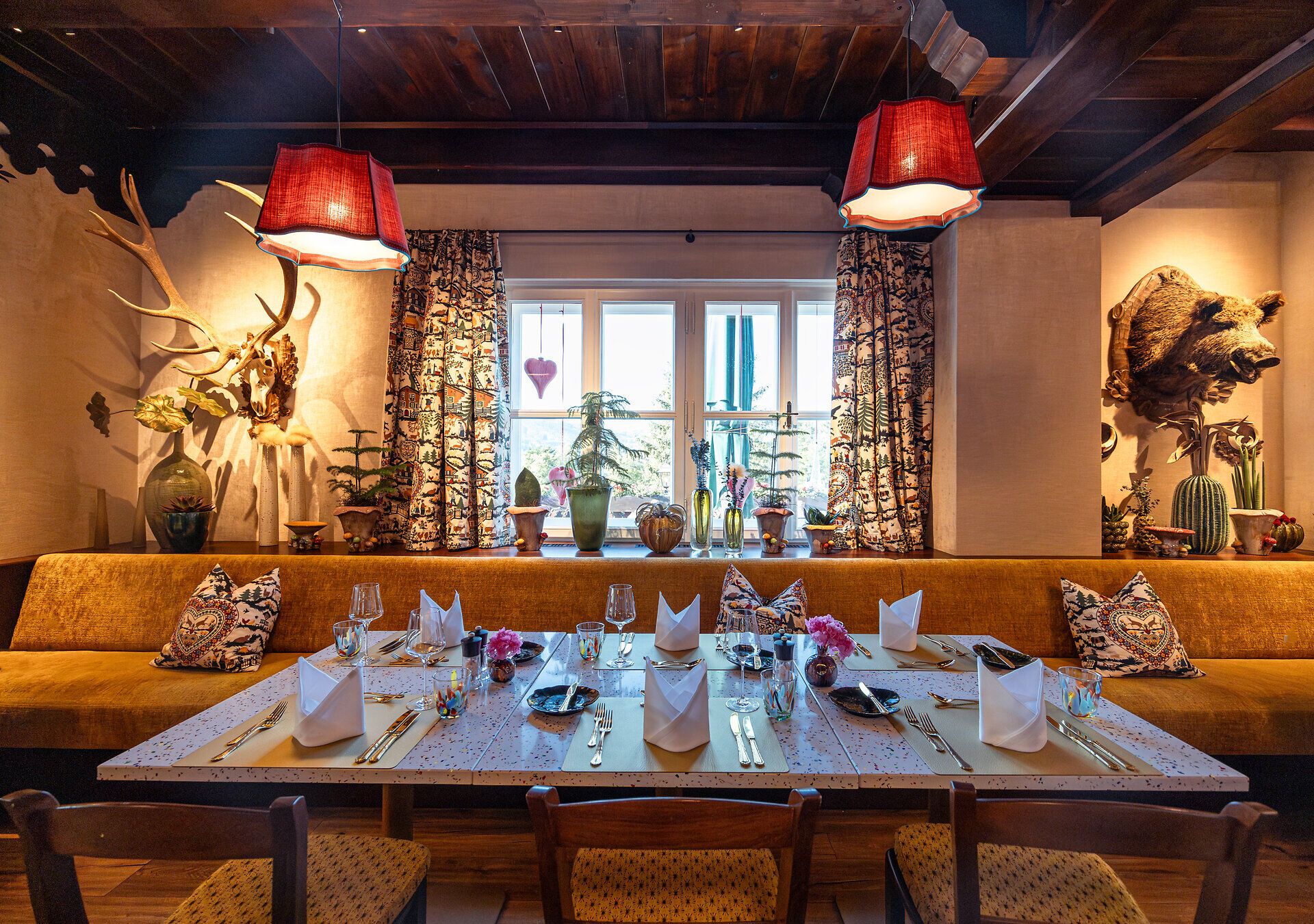 Cozy dining area with large windows, green upholstered furniture and plants, with a view of the countryside.