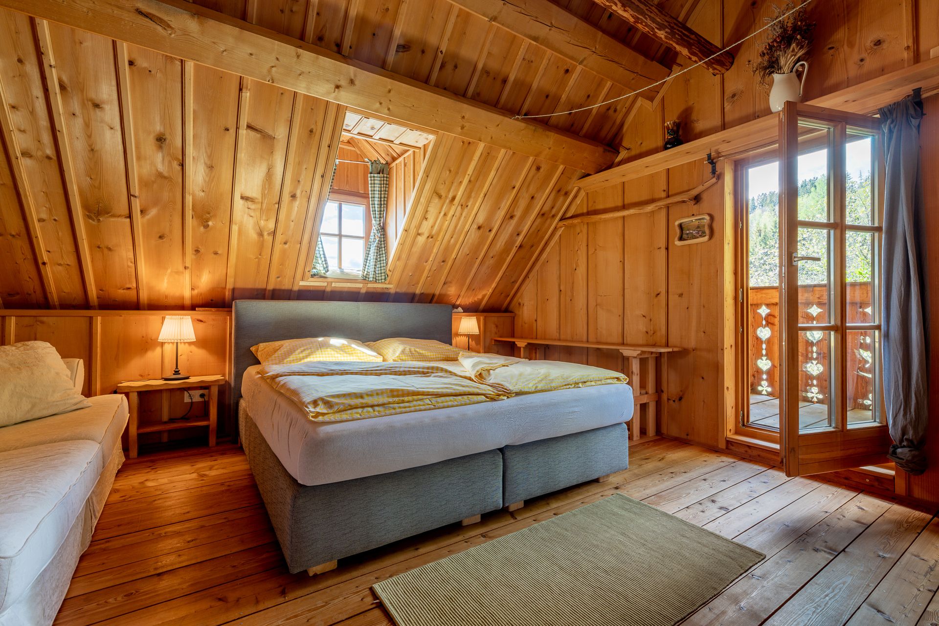 Bedroom with wood paneling, double bed, carpet and open door to the balcony.