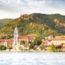 View of D&uuml;rnstein with monastery and castle ruins in front of wooded hills.