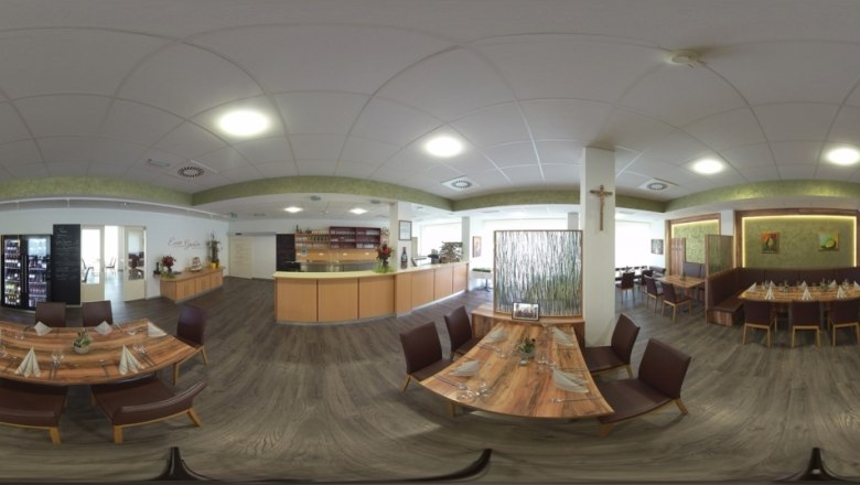 Interior view of a modern restaurant with wooden tables and chairs, decorated with plants and works of art on the walls.
