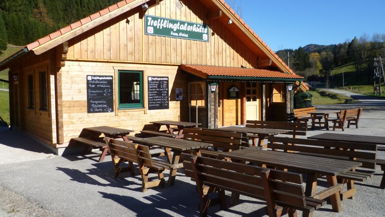 Wooden hut with outdoor tables, sunny day.