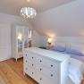 Bright bedroom with double bed, white closet and chest of drawers, wooden floor and modern ceiling lamp.