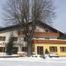 An inn in the snow with wooden decorations and a large tree in front of it.