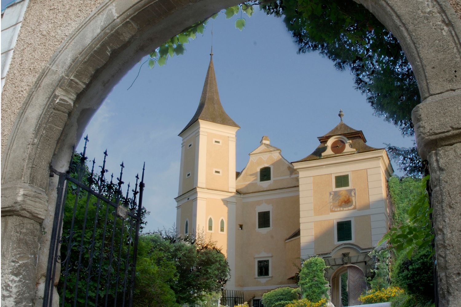 Mühlbach Castle behind a stone archway with a wrought-iron gate.