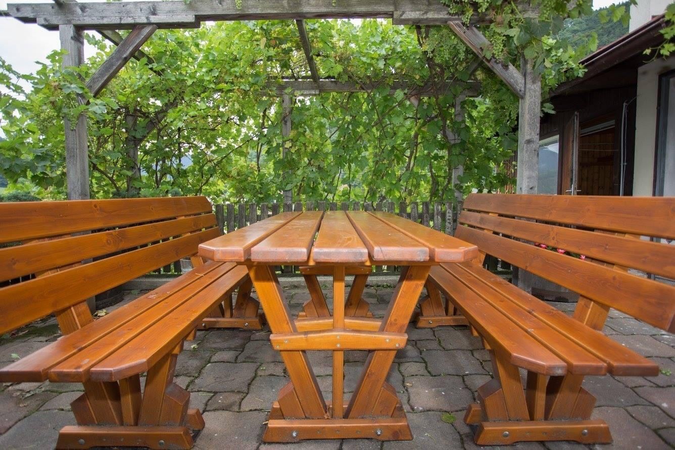 Wooden table and benches outside under a pergola with vines.