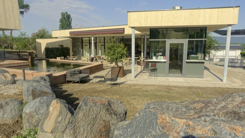 Modern veranda with glass front and seating area, surrounded by rocks and a pond.