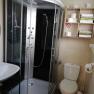 Modern bathroom with shower cubicle, washbasin, toilet and shelf with towels and toilet paper.