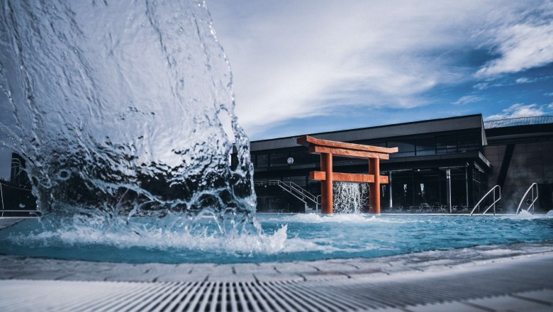 A torii gate in a pool with bubbling water and a modern building in the background.