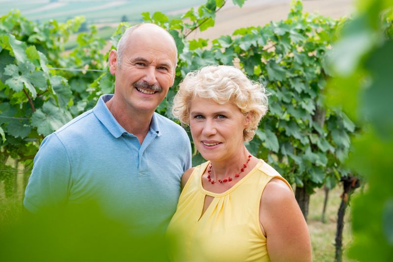 A man and a woman stand smiling in a vineyard.