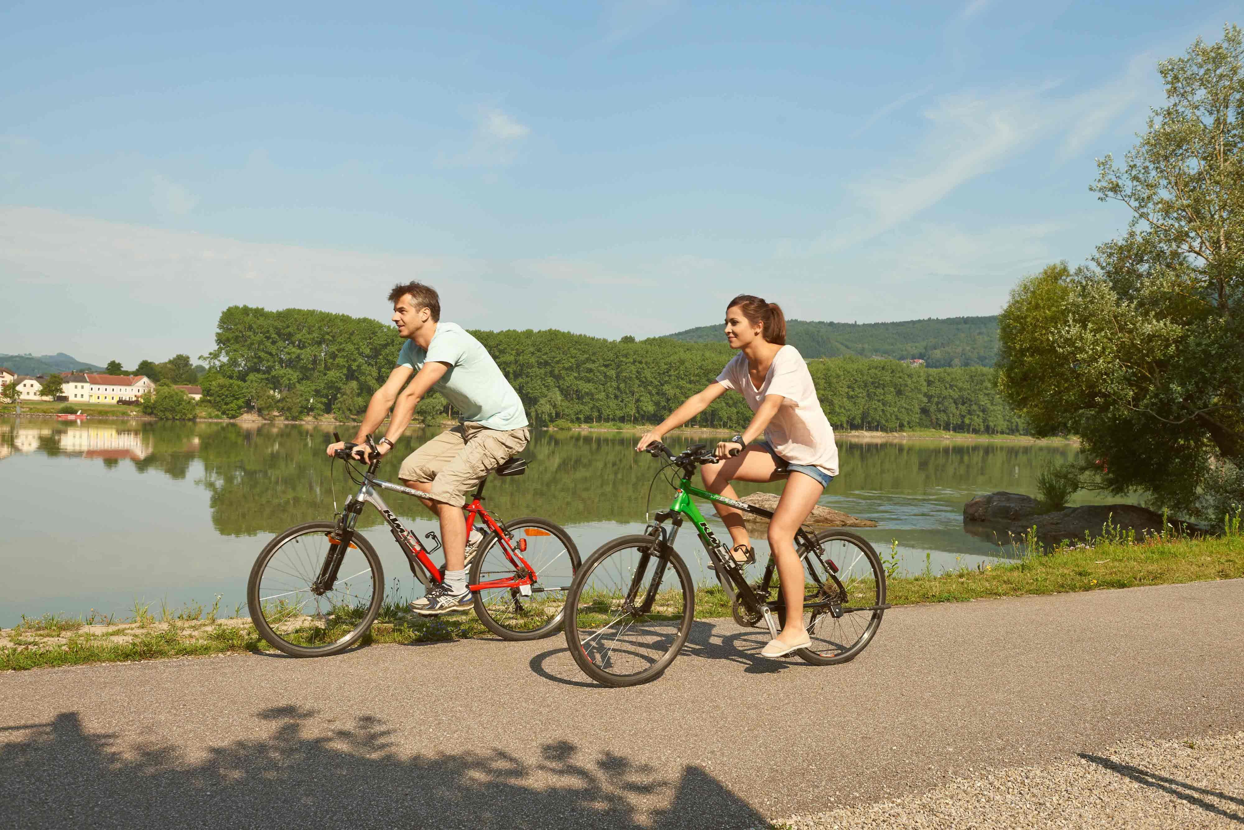 Two cyclists ride on a path along a river in the Nibelungengau.