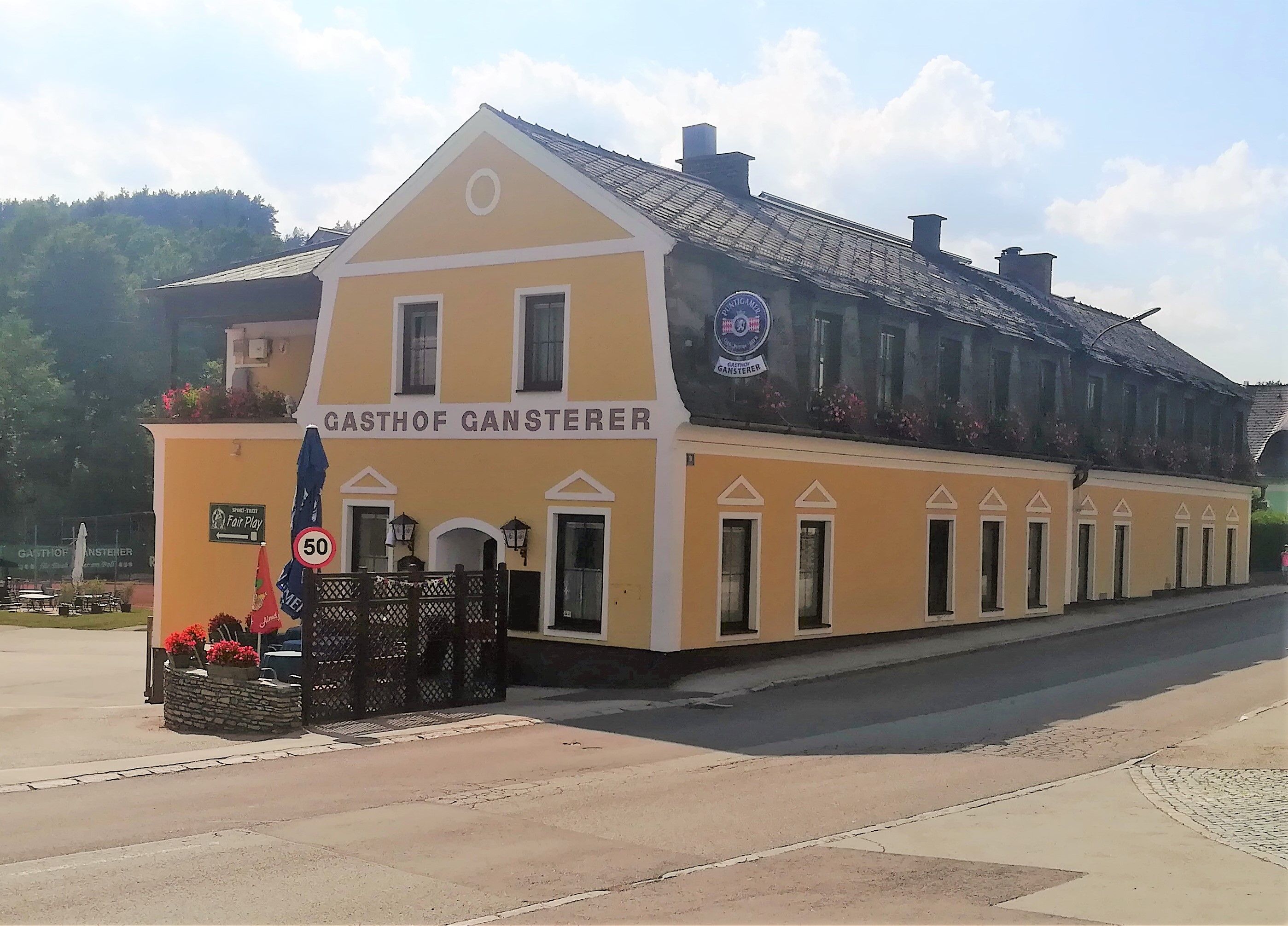 Yellow building of the Gasthof Gansterer in Zöbern with flower boxes and traffic sign.