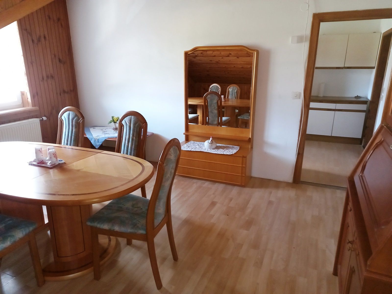 Dining room with wooden table, chairs and mirror, view into the kitchen.