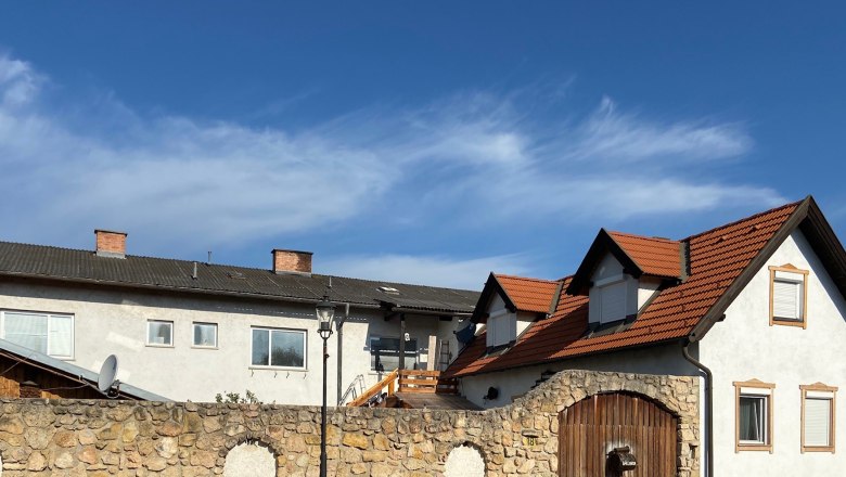 A building with red tiled roofs and a stone wall in the foreground under a blue sky.