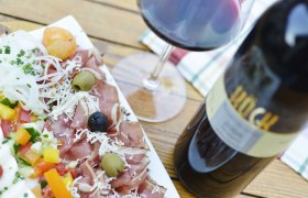 A plate of ham, olives, vegetables and a glass of red wine on a wooden table.