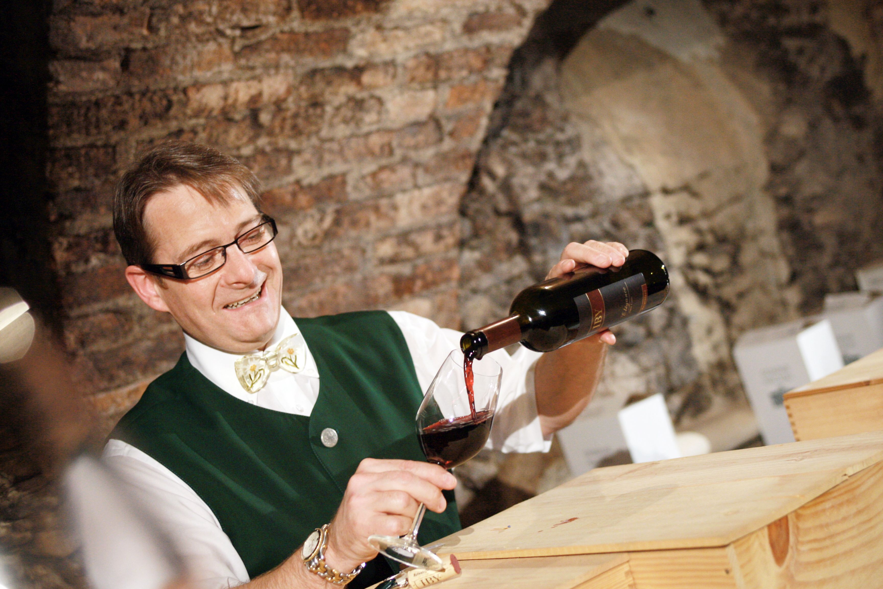 A man in traditional dress pours red wine into a glass.