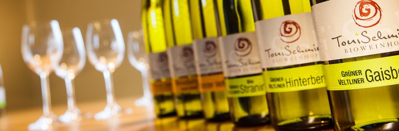 Row of wine bottles with glasses in the background.