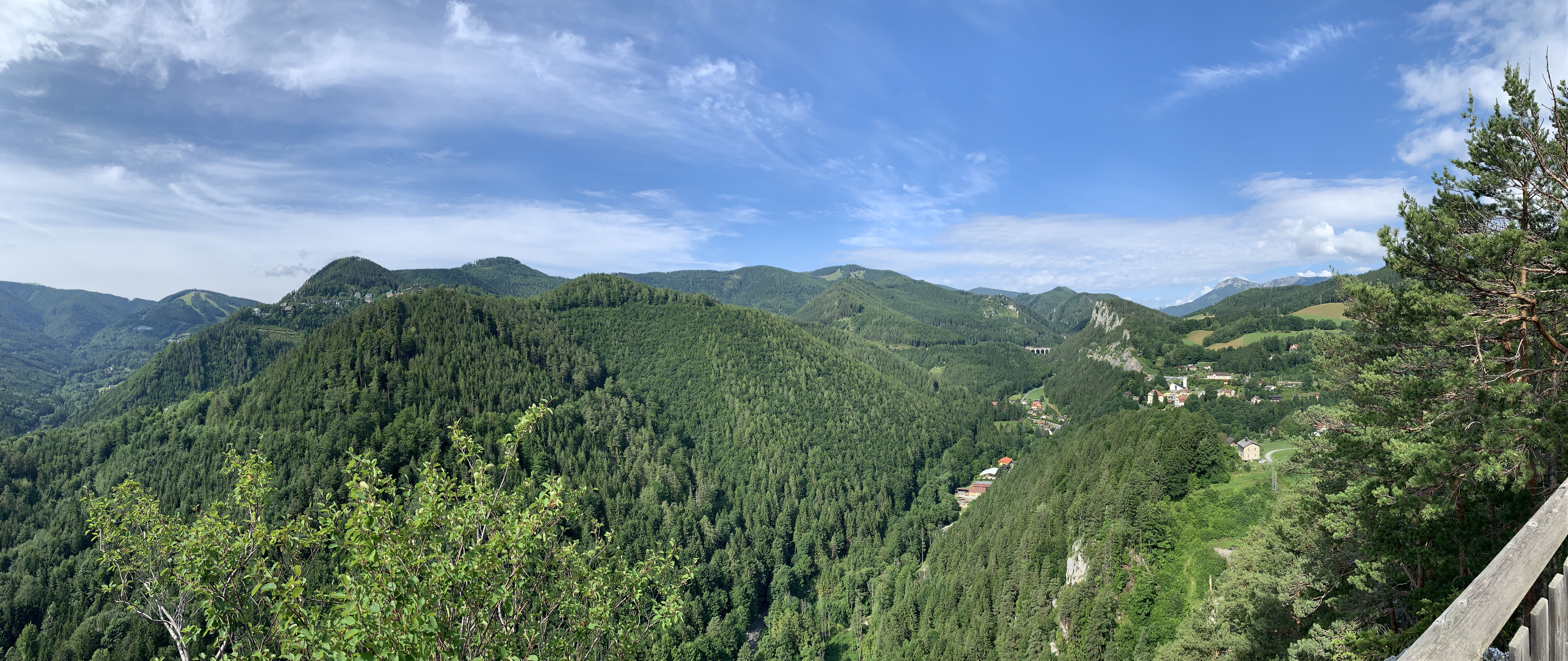Panoramic view of wooded hills and a valley with scattered houses under a blue sky.