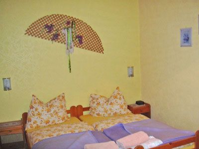 A cozy bedroom with yellow walls, a double bed with patterned pillows and a decorative wall fan.