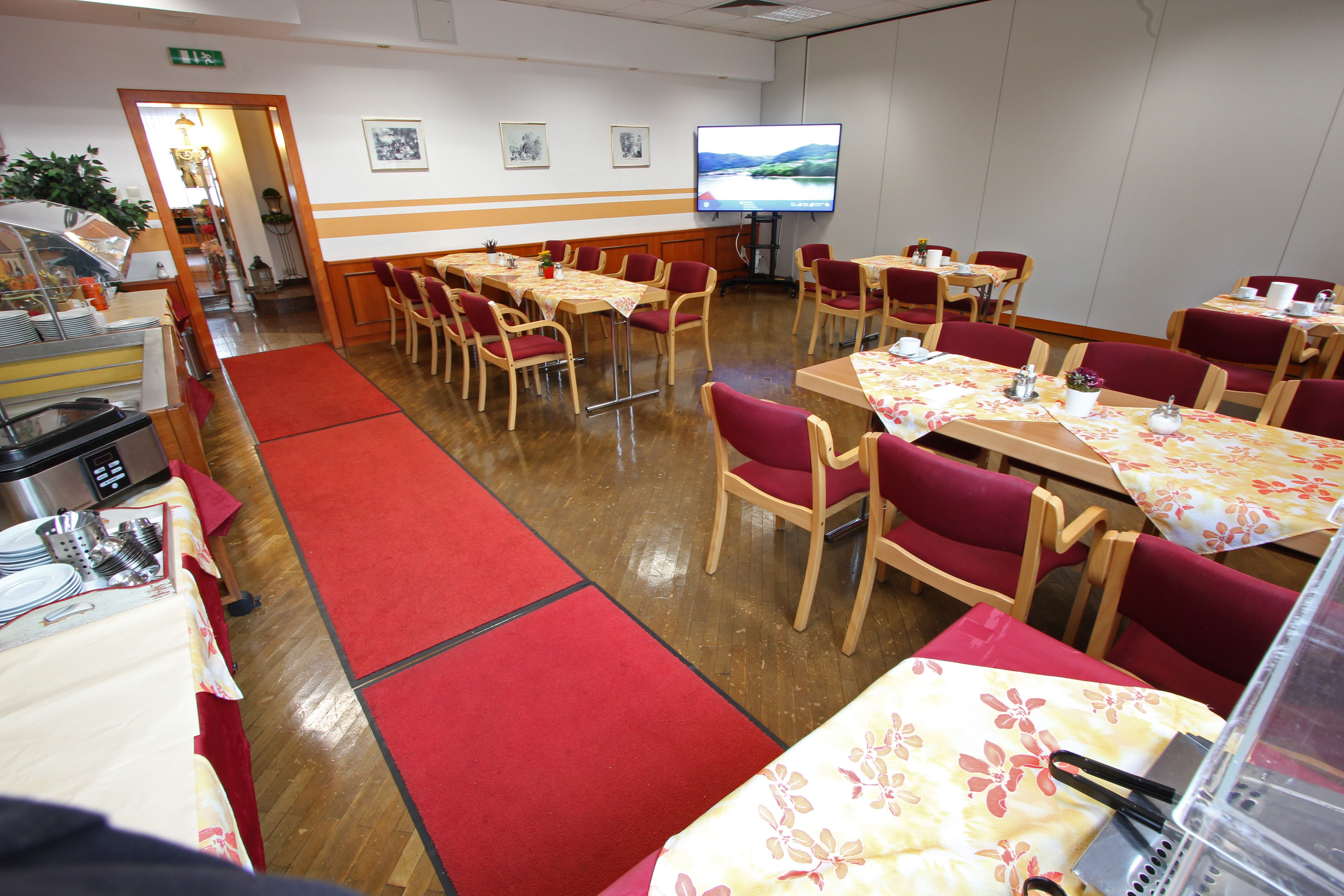 A conference room with covered tables, red chairs and a large screen.