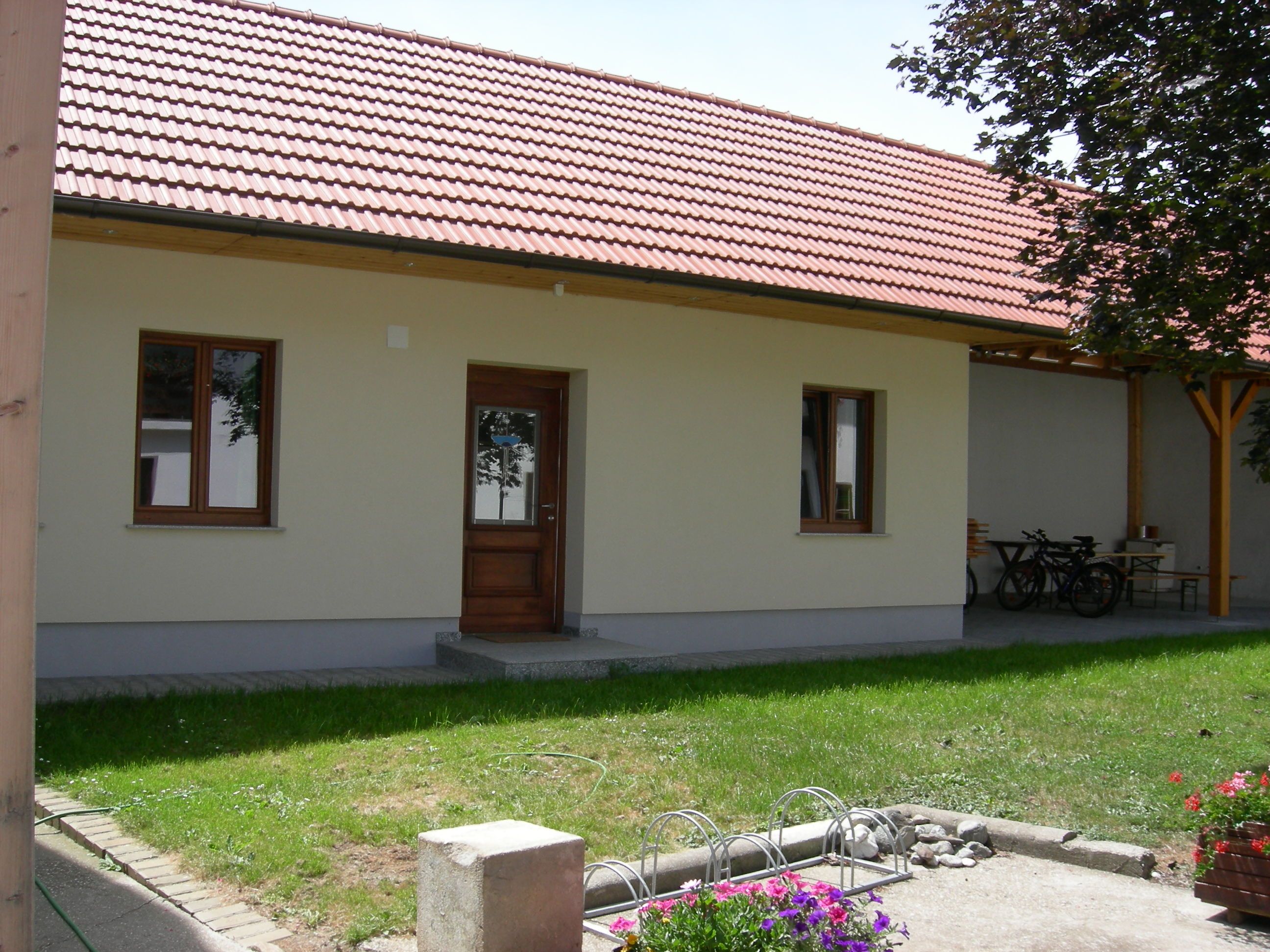 An inner courtyard with a building with a red tiled roof, wooden door and windows. Flowers and a bicycle stand can be seen in the foreground.