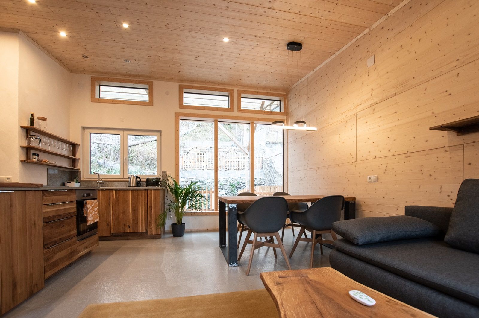 Modern living and dining area with wooden furniture and large windows.