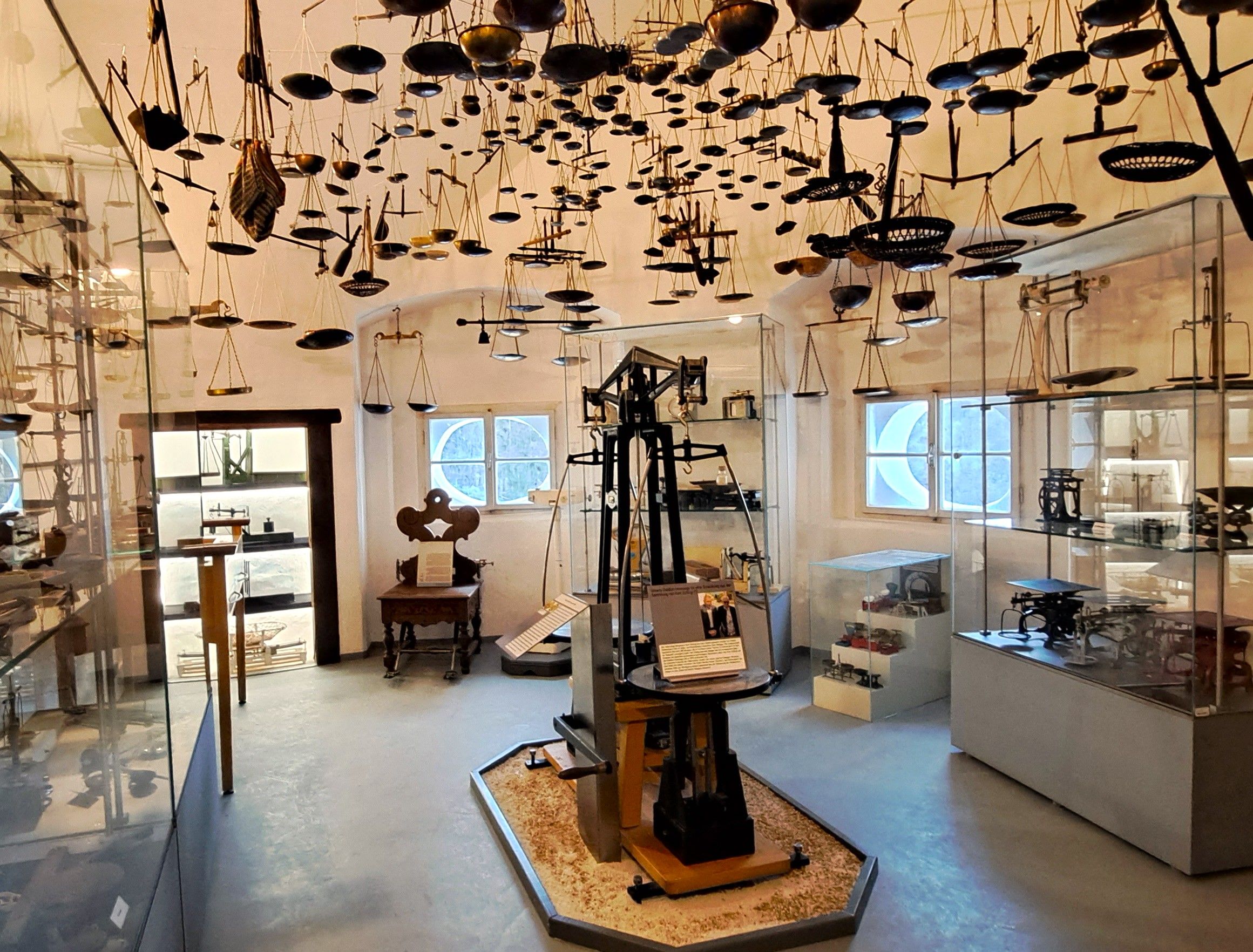 Interior view of the Austrian Scales Museum with numerous scales on the ceiling and in display cases.