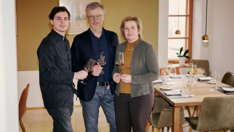 Three people standing in a restaurant holding glasses of wine
