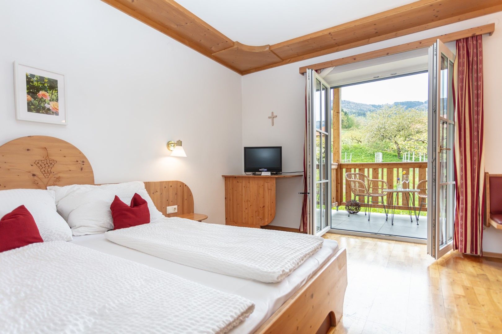 A cozy double room with wooden furniture, a balcony with a view of the countryside and a small TV.