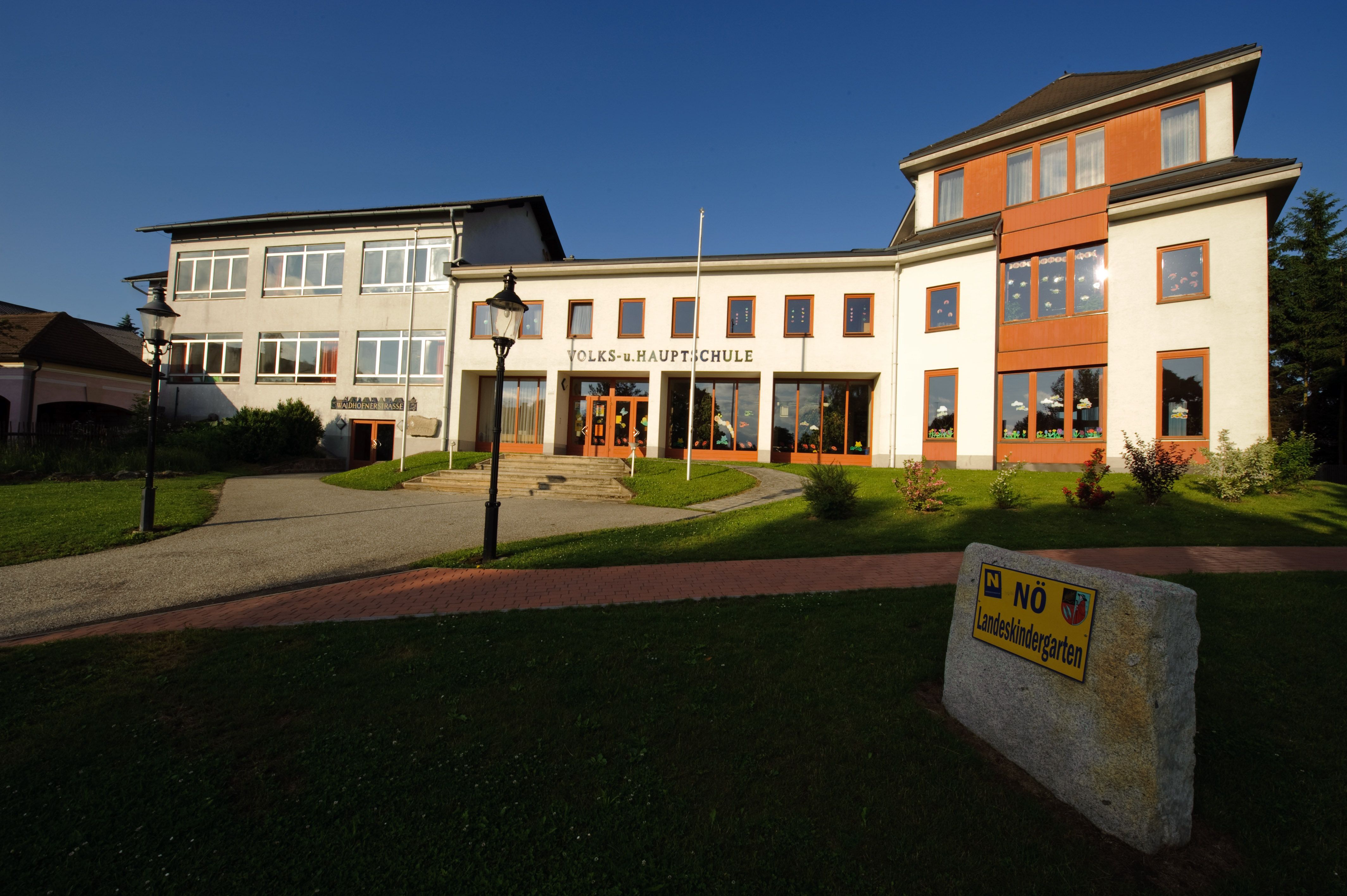 Building of the Kautzen primary and secondary school with a well-tended lawn and a sign for the state kindergarten.