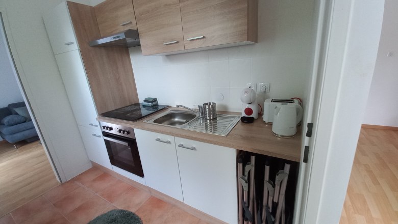 Modern kitchenette with wooden and white units, stove, sink and kitchen appliances.