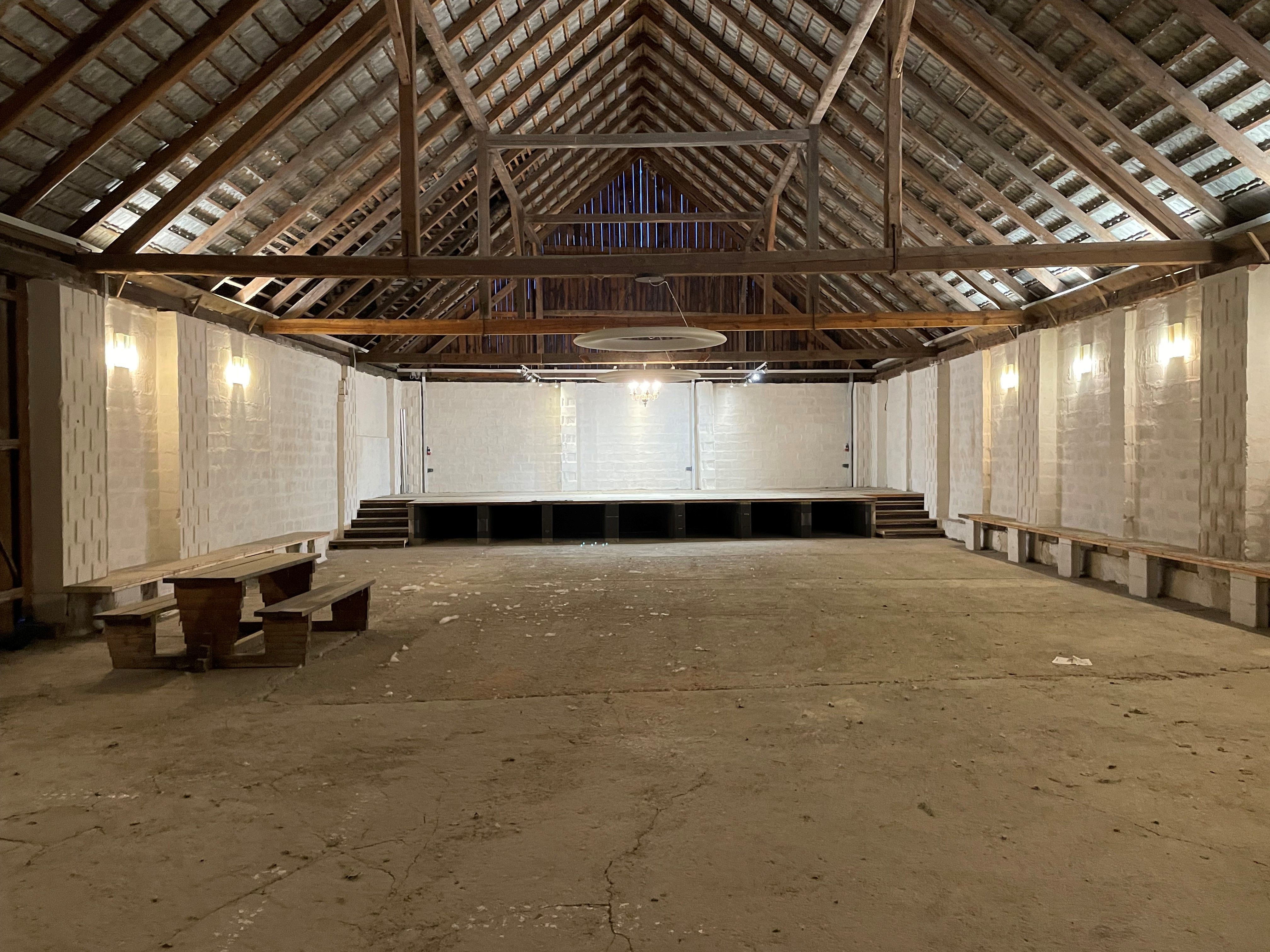 Interior view of an empty barn with a wooden roof and a stage.