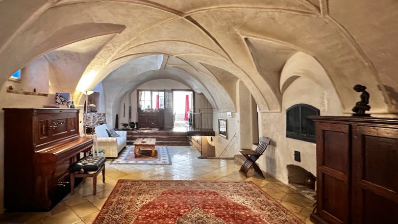 Historic reception hall with vaulted ceiling, carpet, piano and wooden furniture.