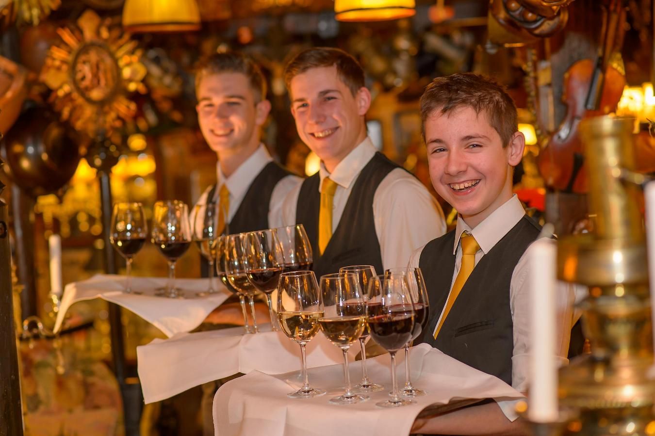 Three waiters in a restaurant with trays full of wine glasses.