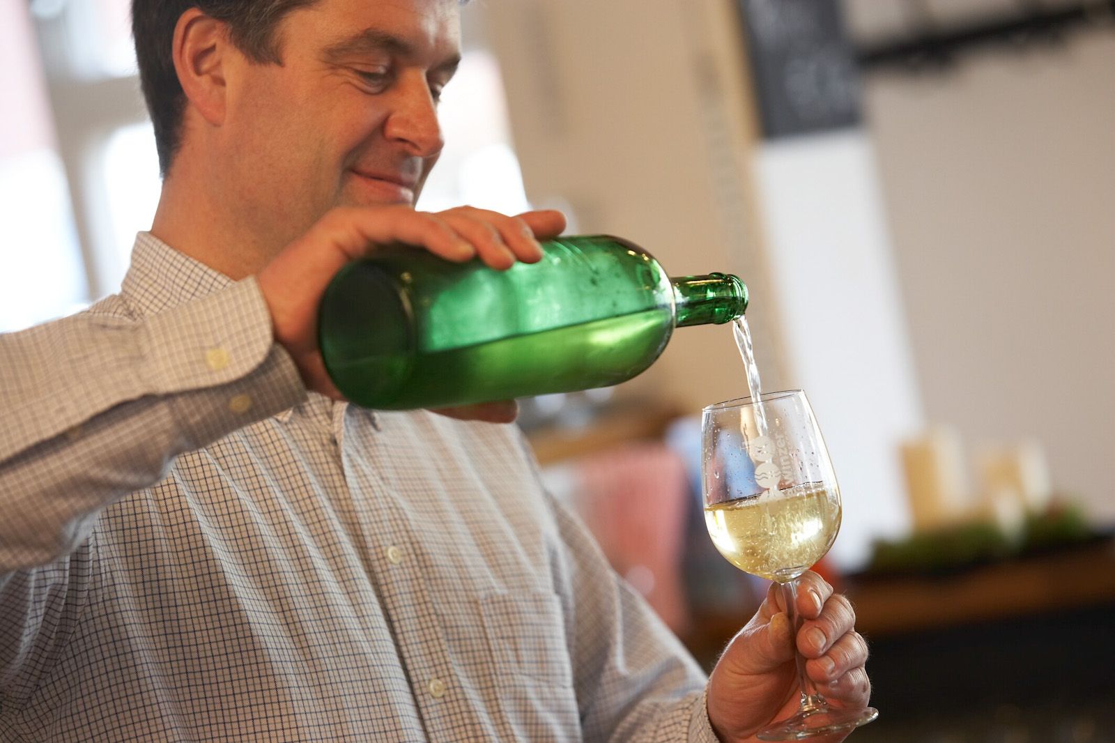 A man pours white wine from a green bottle into a glass.