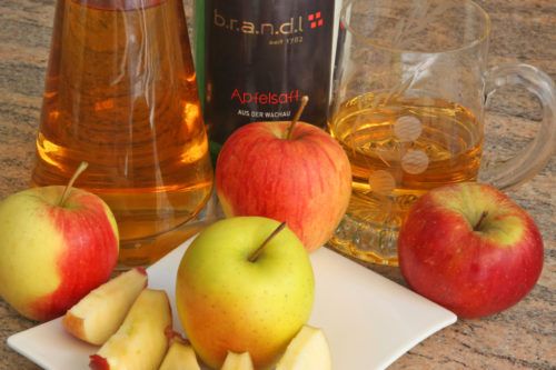 Different types of apples and apple juice on a table.